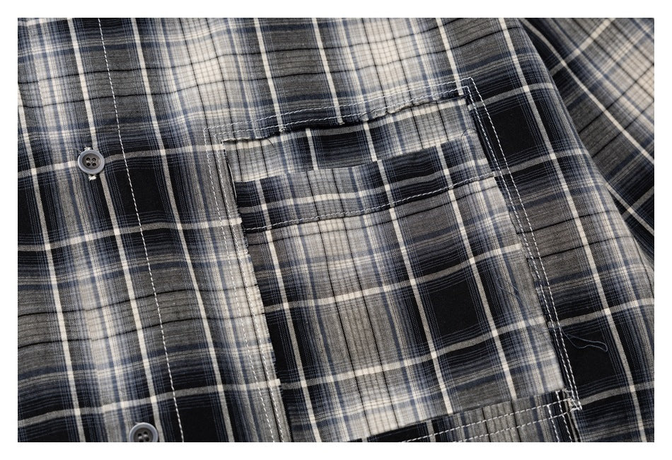 Close-up of a large chest pocket, stitching, and buttons on a black, gray, and cream plaid shirt.