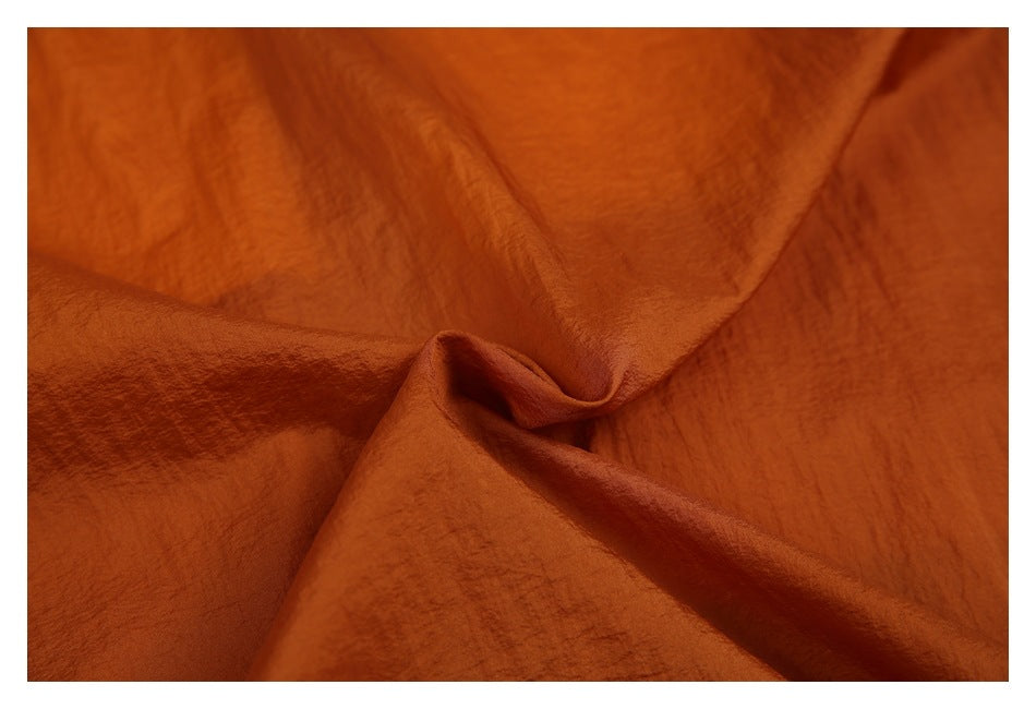 Close-up of rust-orange fabric draped into folds, showing its surface texture.