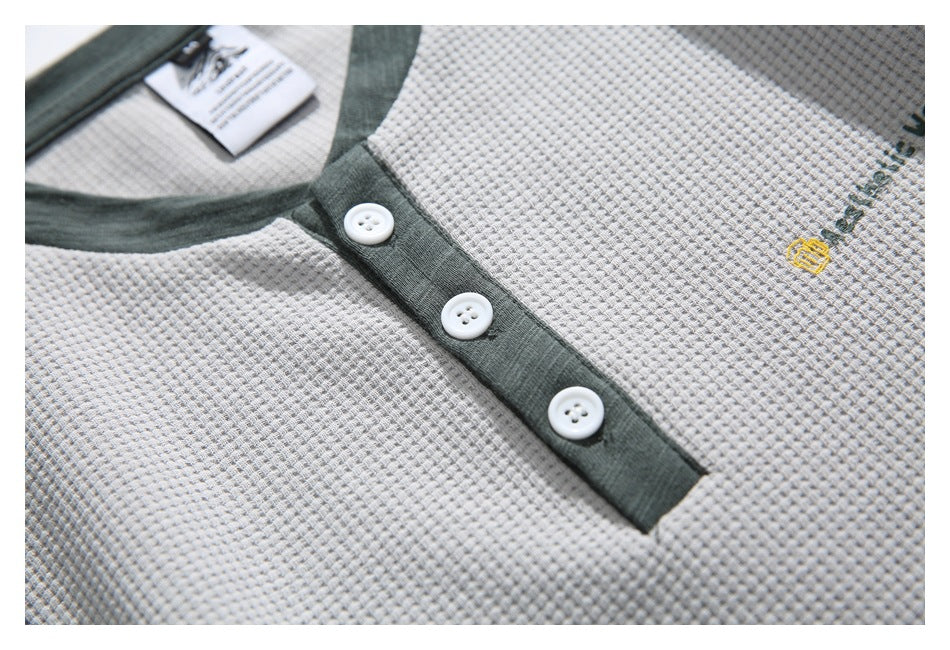 Close-up of a light gray waffle-knit shirt showing its dark green three-button placket and small embroidered chest emblem.