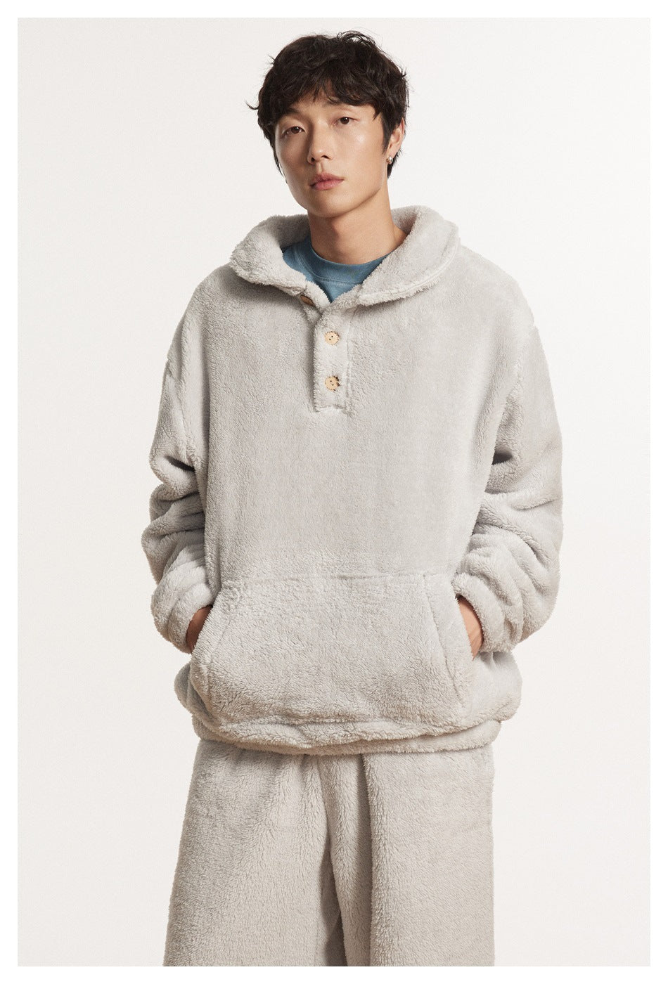 Close-up of a model in a gray plush pullover with button placket and kangaroo pocket over a blue tee