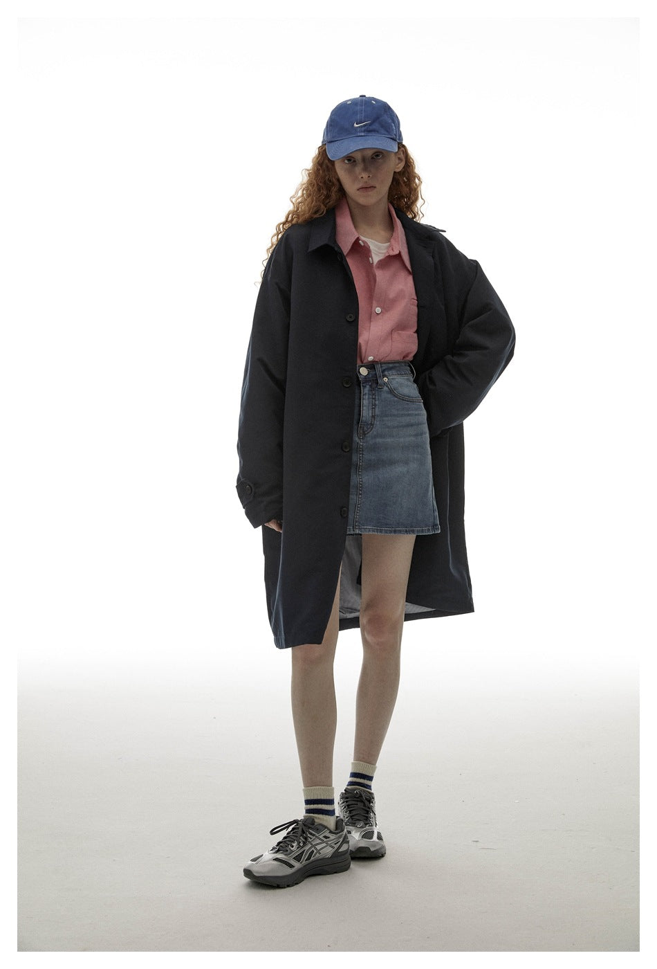 Model in the navy oversized coat worn open with one hand in the pocket, over a pink shirt and denim skirt