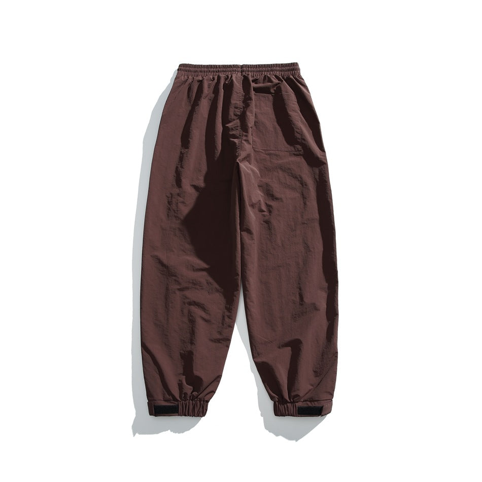 Back view of brown loose jogger pants laid flat, with an elastic waist, a rear patch pocket, and adjustable ankle cuffs.