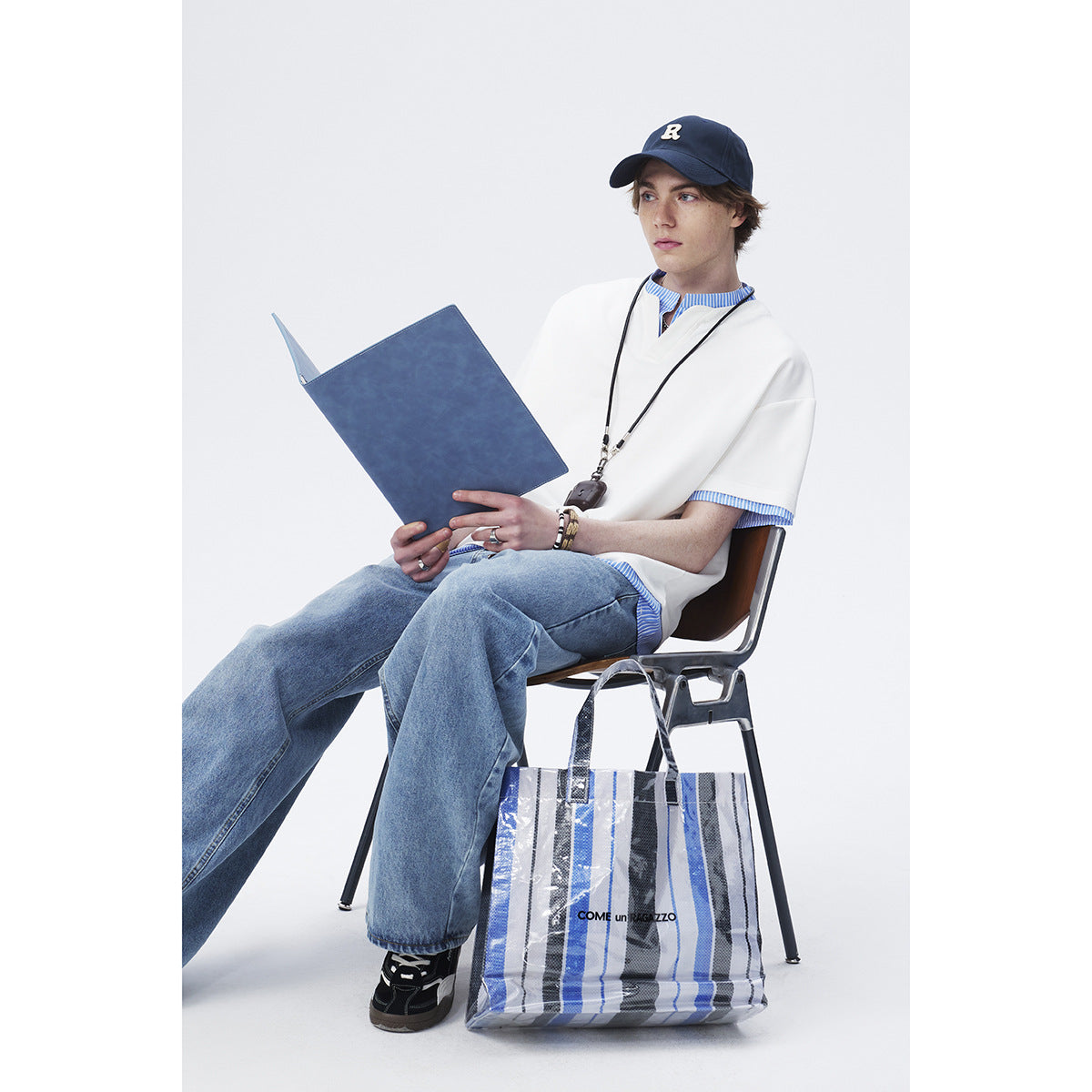 Model seated in an oversized white short-sleeve top with a notched neckline and blue striped trim.