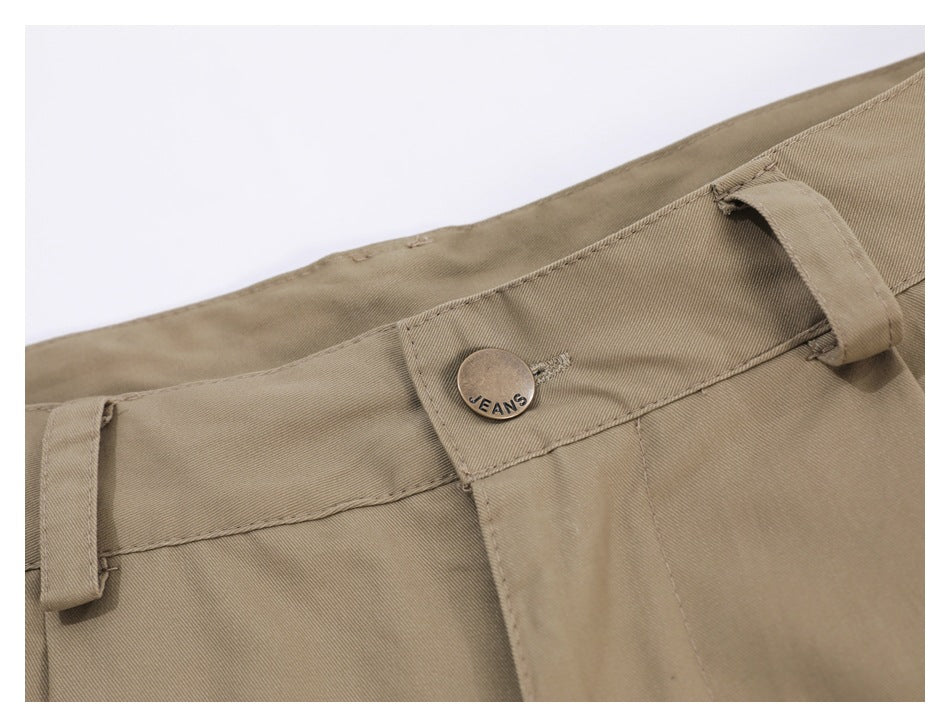 Close-up of a khaki trouser waistband with belt loops and a metal button marked JEANS.