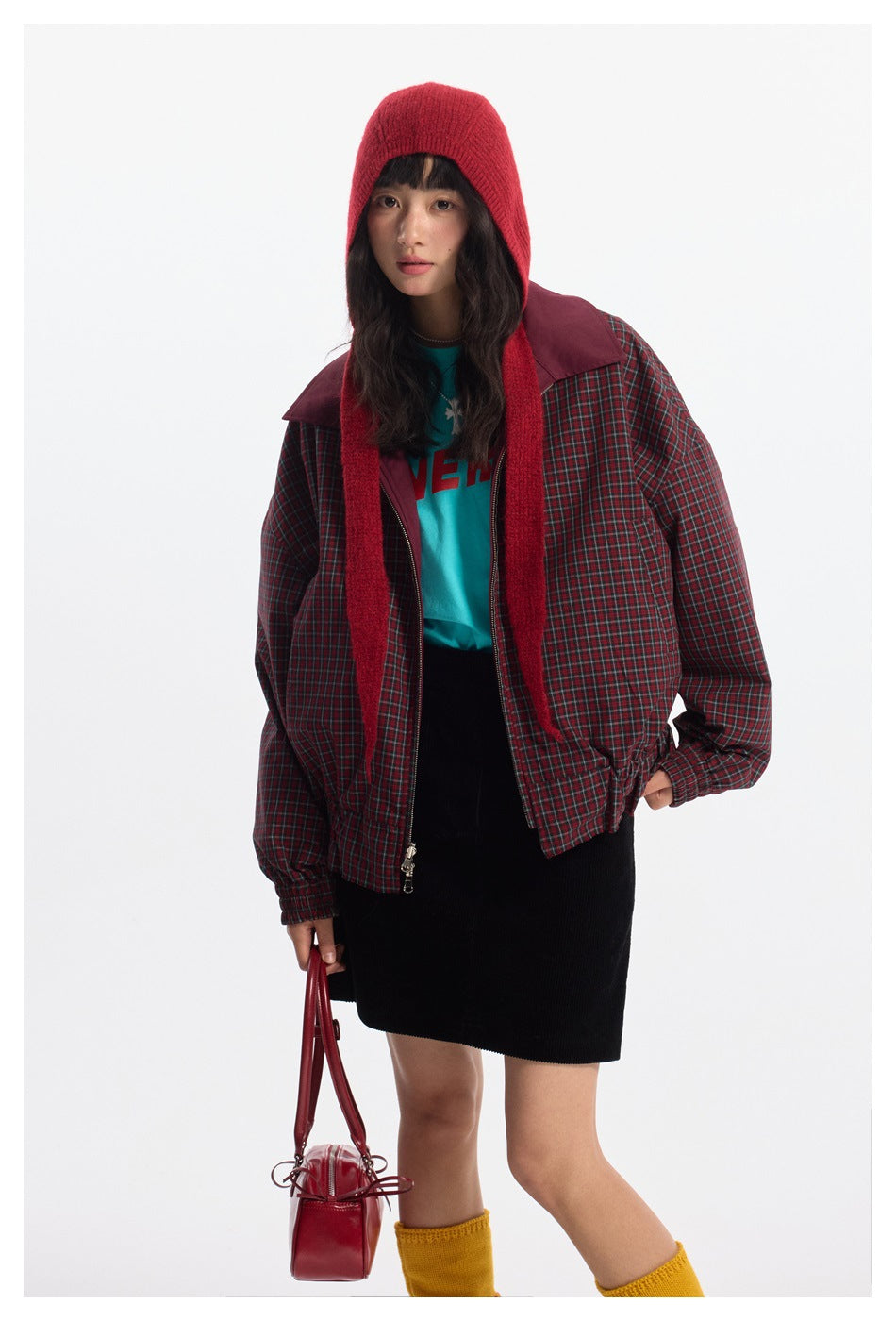 Closer front view of a model in a red-and-green plaid jacket with burgundy panels, worn open over a turquoise top.