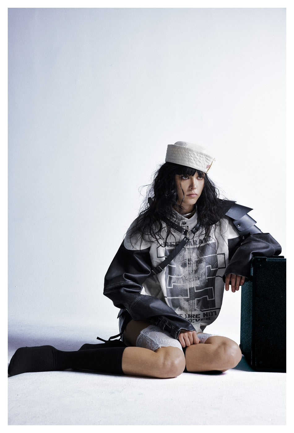 Model wearing an off-white graphic jacket with black sleeves and sculpted shoulder panels, paired with a white cap and lace