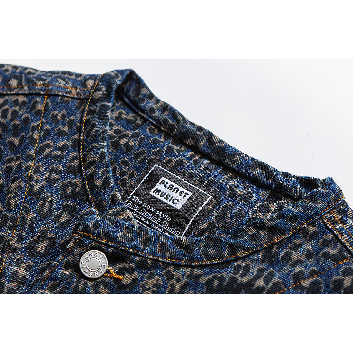 Close-up of a blue and charcoal leopard-print denim jacket collar, orange stitching, metal button, and sewn-in label.