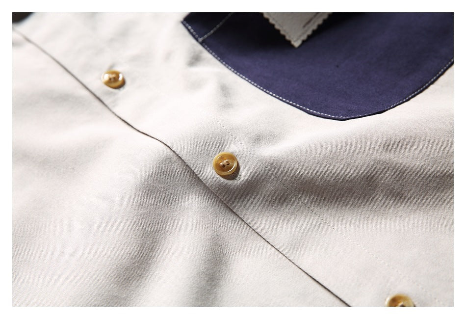 Close-up of tan buttons, stitching, and the edge of a navy pocket on a light beige shirt.