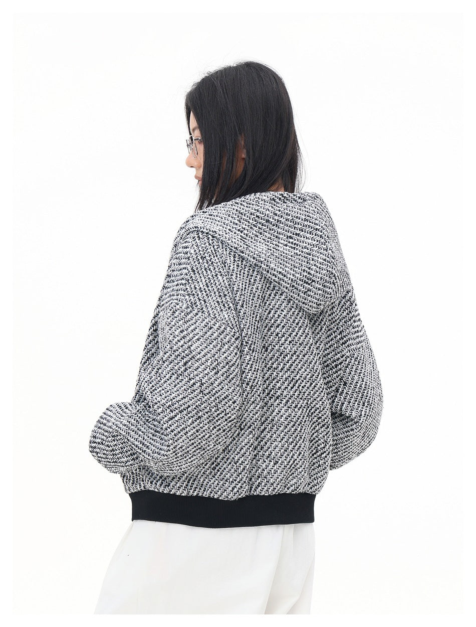 Rear three-quarter view of a model wearing a black-and-white patterned hooded jacket with a black ribbed hem.