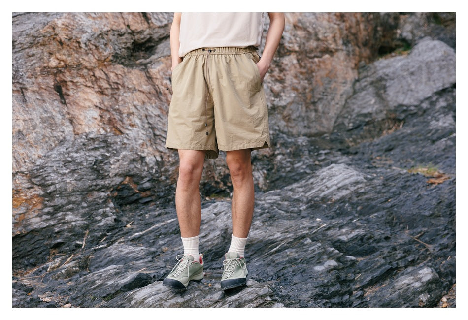 Model wearing tan drawstring shorts with side pockets, shown from the front against a rocky outdoor backdrop.