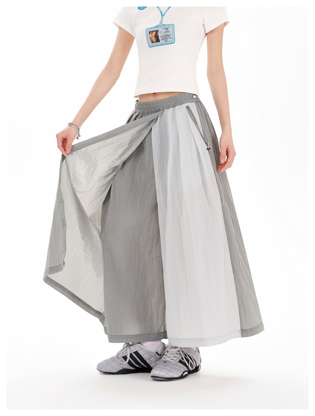 Model lifts a panel of gray-and-white wide-leg bottoms to show the contrasting sections and zip pocket.