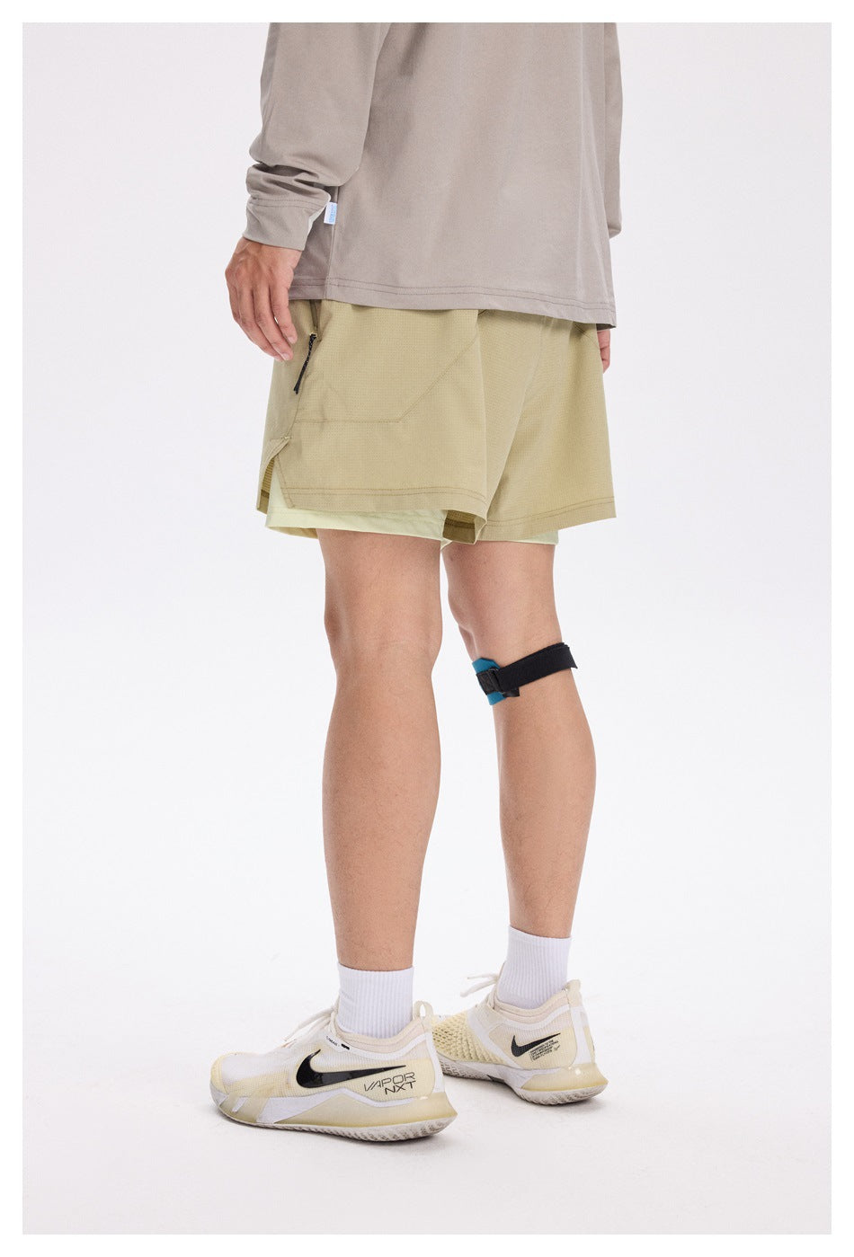Side-rear view of a model wearing khaki layered running shorts with a zip pocket.