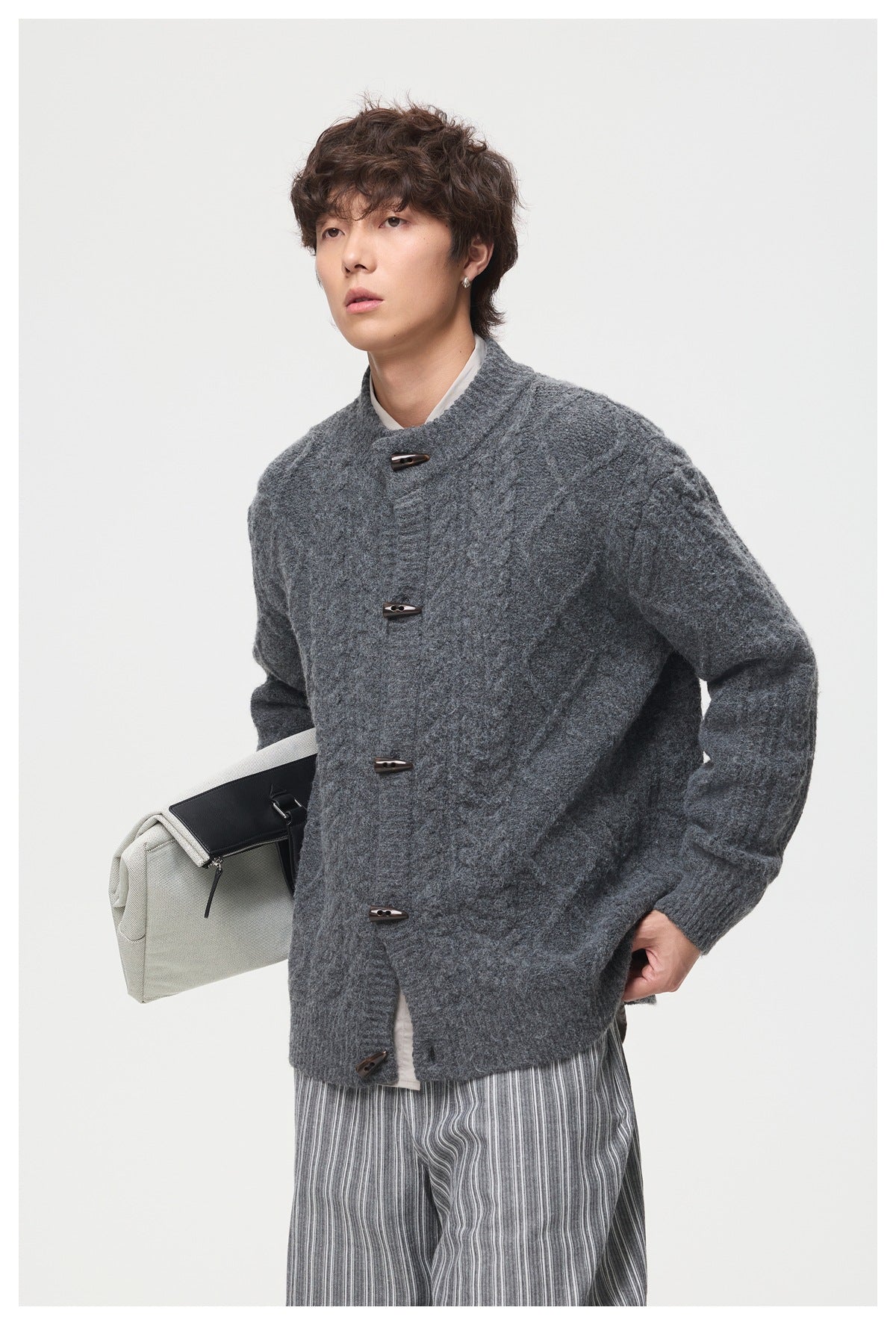Closer front view of a model in a charcoal cable-knit cardigan with a stand collar and toggle buttons.