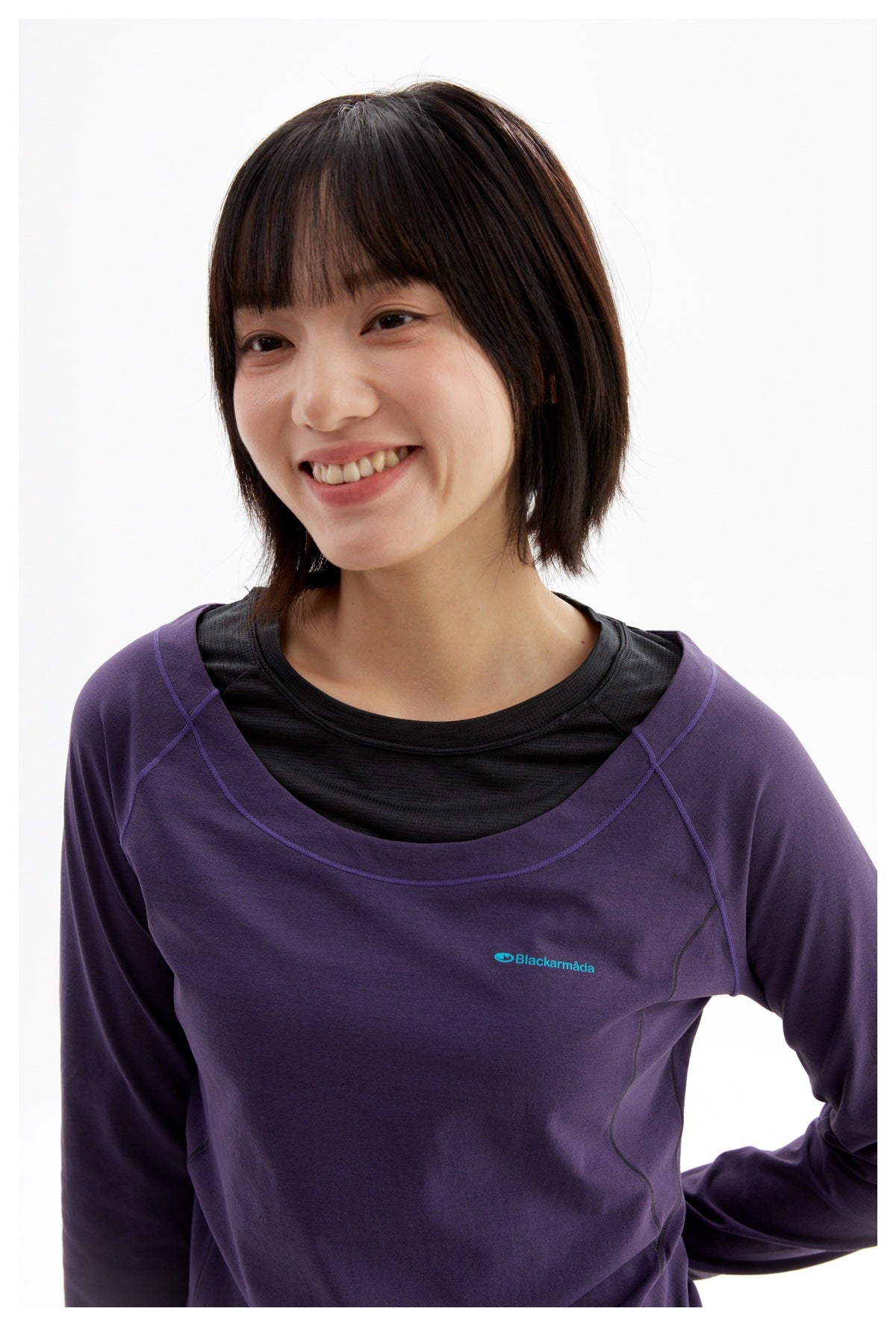 Close-up of a model wearing a purple top over a black shirt, showing the layered neckline and chest logo.