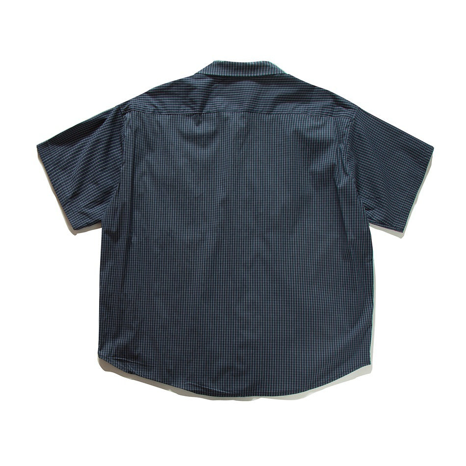 Back view of a dark short-sleeved button-up shirt with a fine grid pattern and a curved hem.