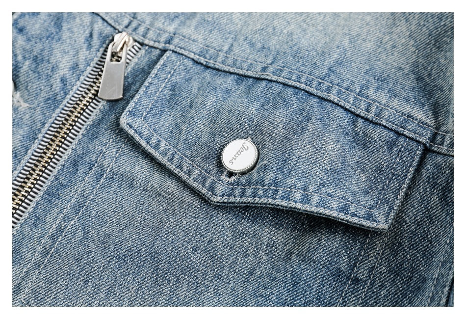 Close-up of a light blue denim jacket flap pocket with a silver button and zipper.