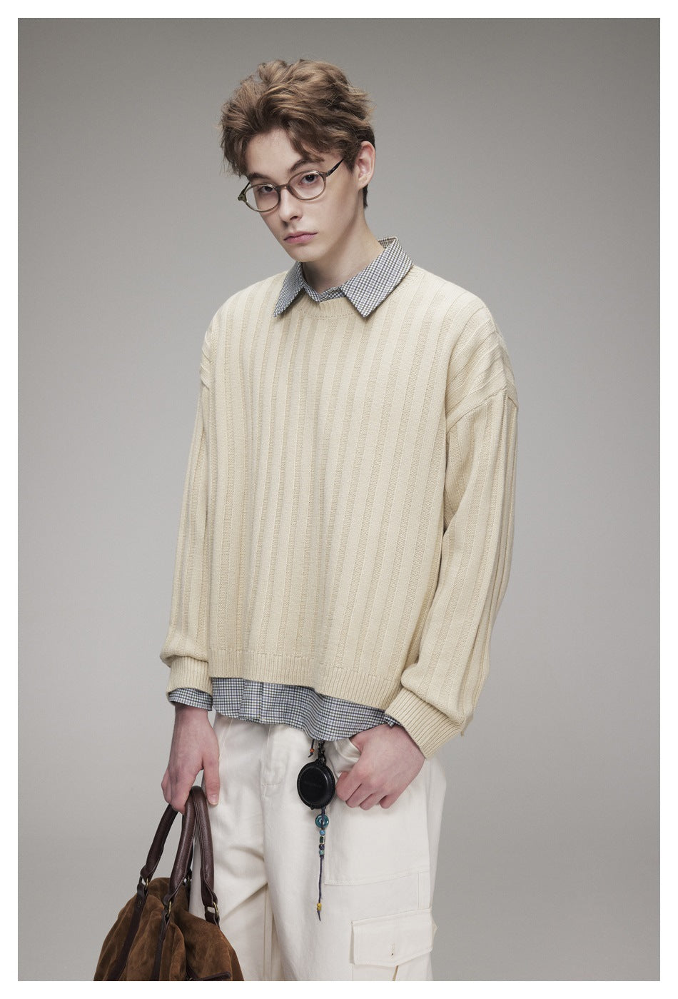 Closer view of a model wearing a cream ribbed sweater layered over a checked shirt.