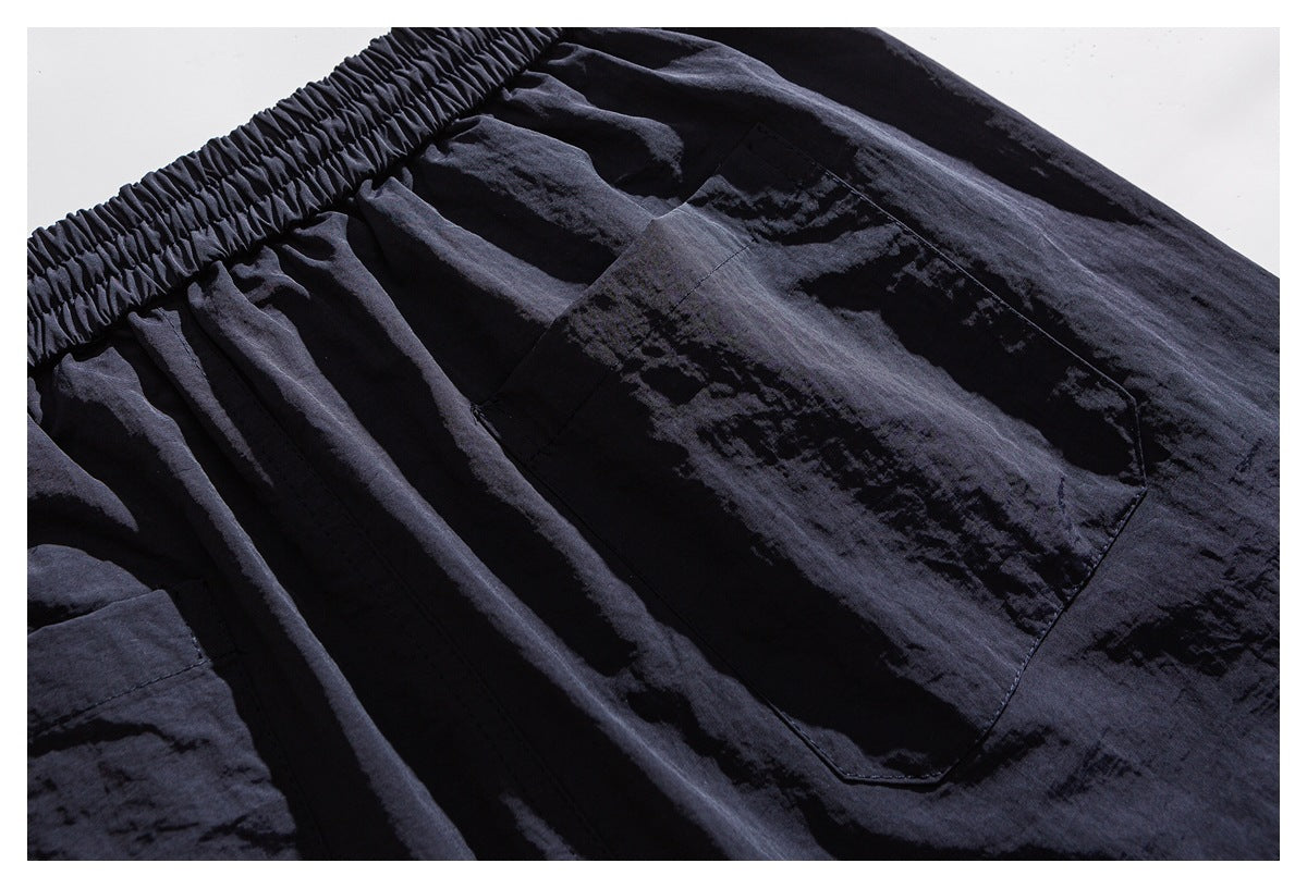 Close-up of dark shorts showing a large stitched patch pocket below the elastic waistband.