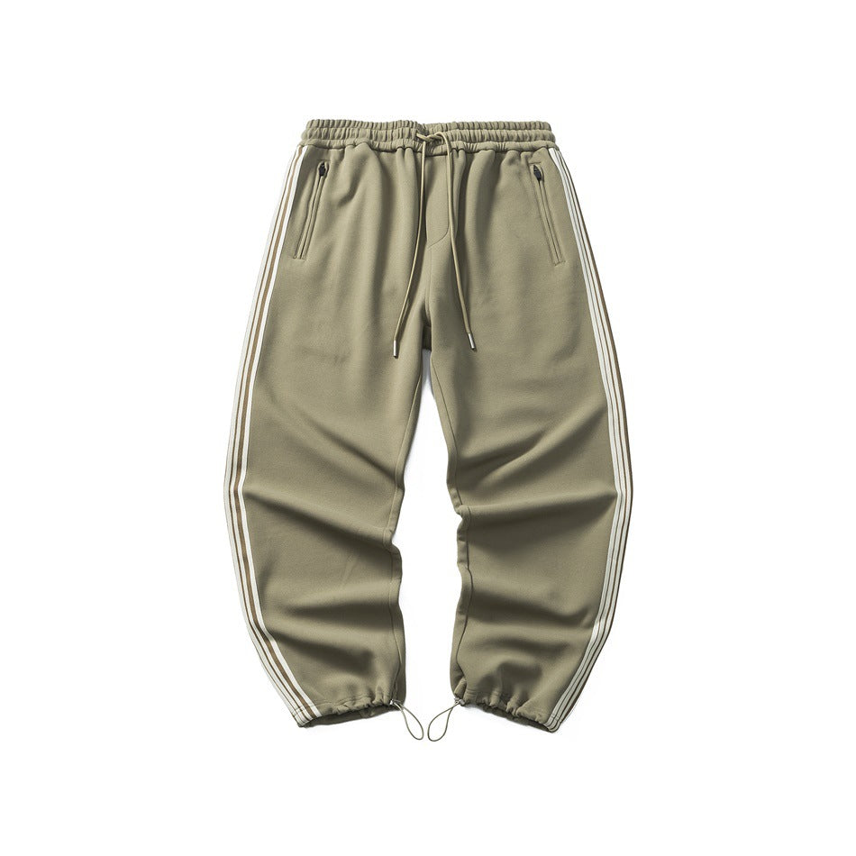 Dark khaki drawstring jogger pants with zip pockets and cream and brown side stripes, flat lay front view