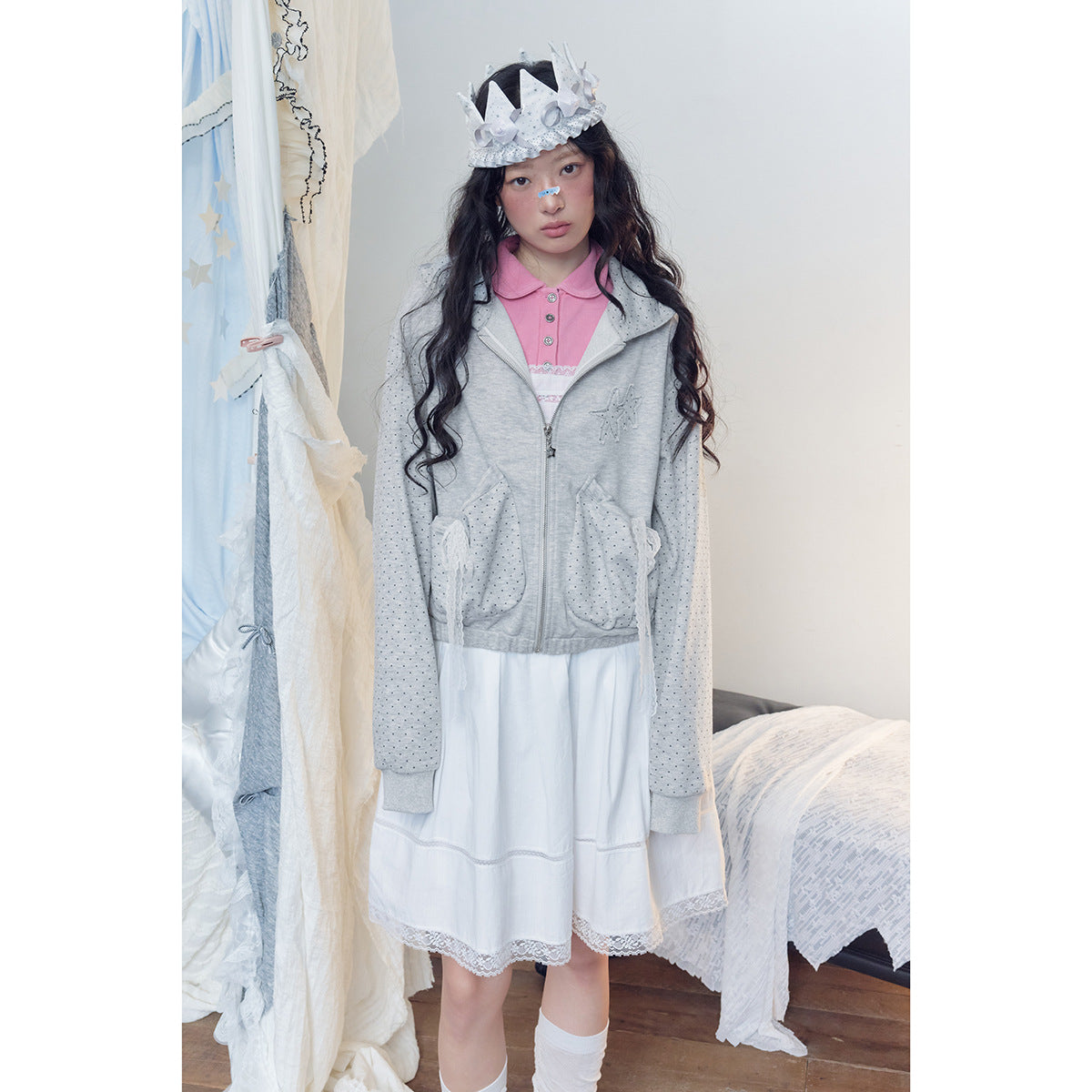 Model wearing a zipped light gray dotted hoodie with lace-trimmed pockets over a white dress and pink collared top.