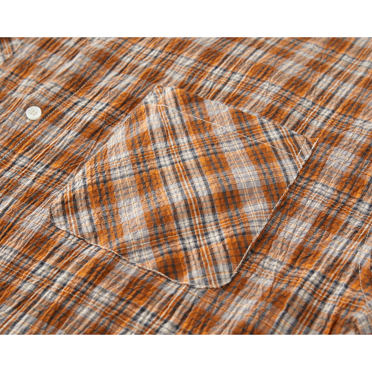 Close-up of a patch pocket on an orange, gray, and cream plaid shirt.
