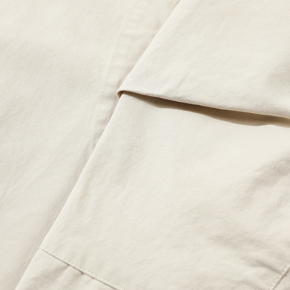 Close-up of off-white jacket fabric, a folded panel, and stitched seams.