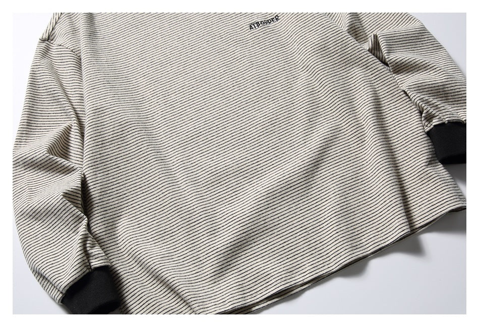 Angled close-up of the off-white shirt's fine dark stripes, chest embroidery, and black ribbed cuffs.