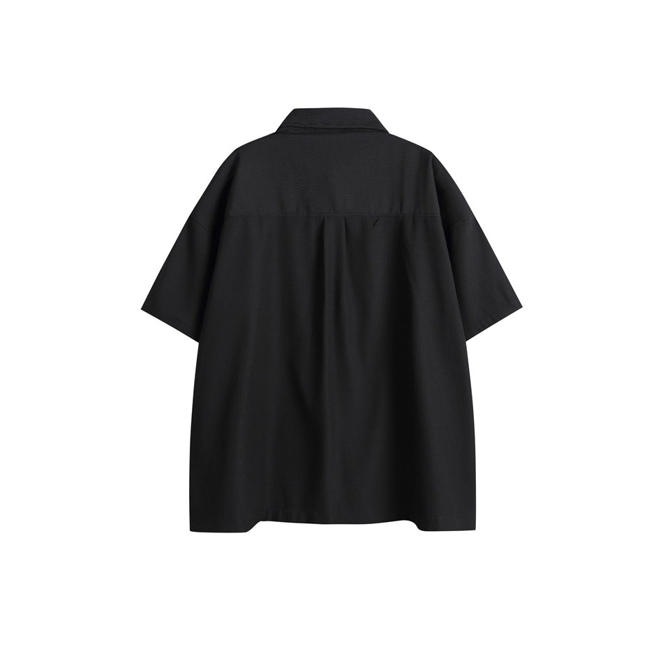 Back view of a black short-sleeve collared shirt with a yoke seam and center pleat.
