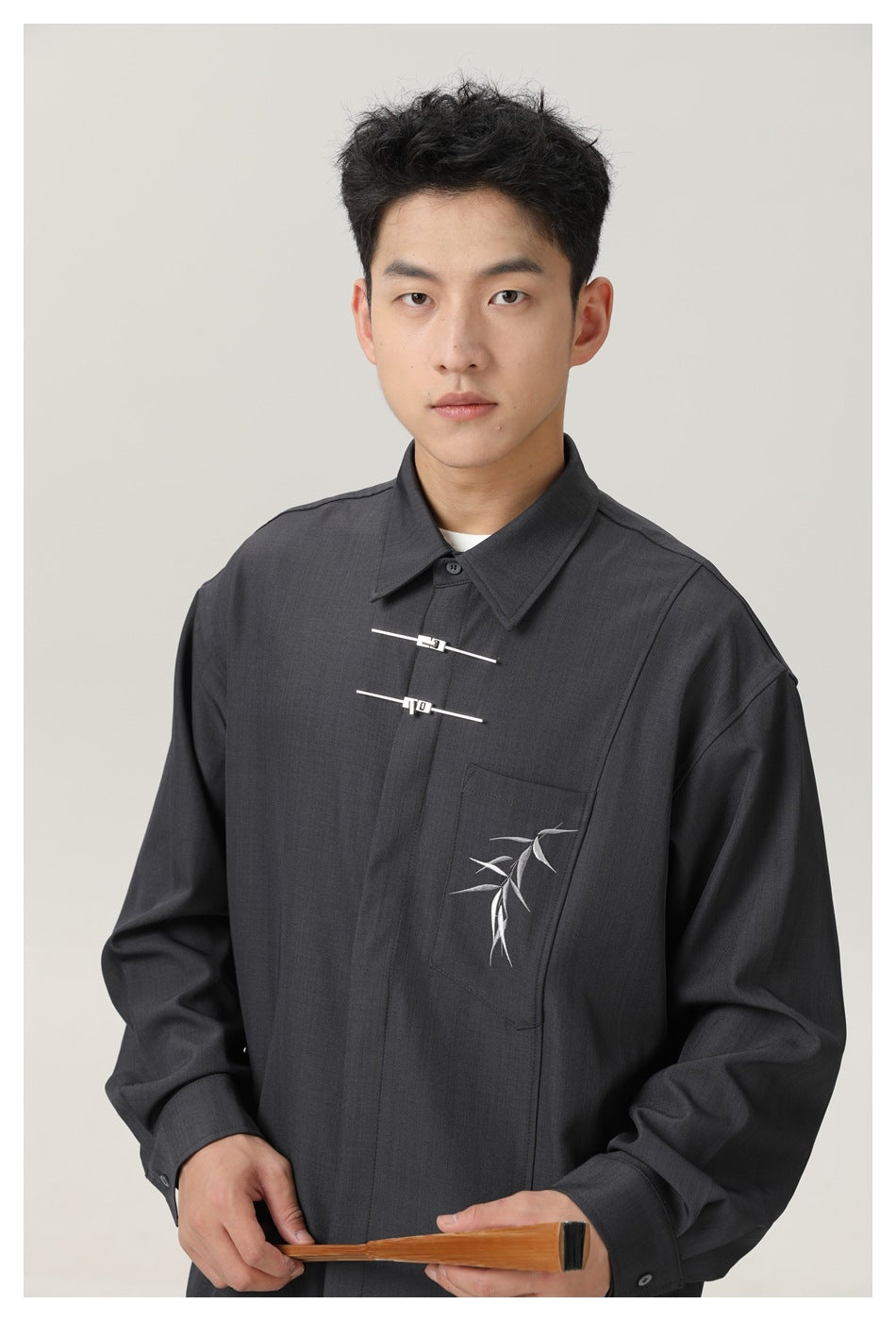 Upper-body view highlighting the charcoal shirt’s pointed collar, two metal front fasteners, and embroidered bamboo chest
