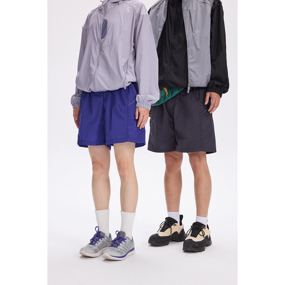 Two models wearing the shorts in royal blue and dark charcoal, with lightweight jackets.