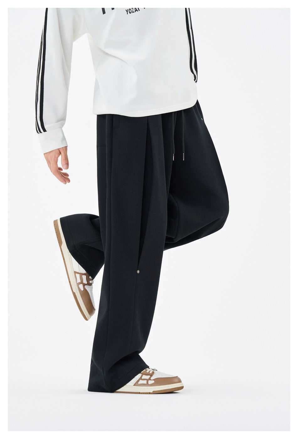 Side view of a model wearing loose black wide-leg trousers with a snap-button panel and drawstring waist.
