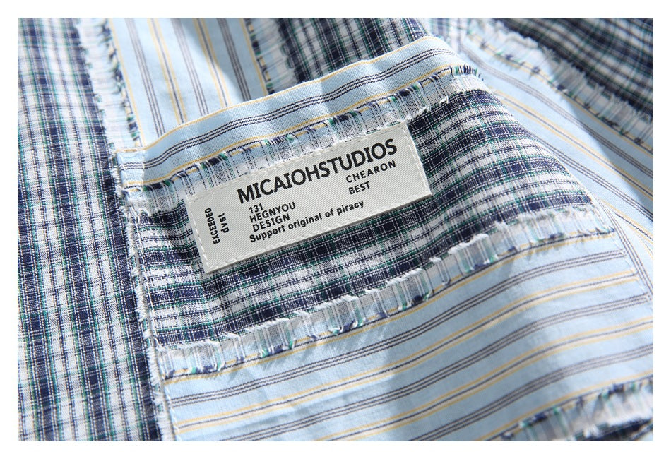 Close-up of the shirt’s chest pocket and sewn label with English lettering against a blue-gray plaid pattern.