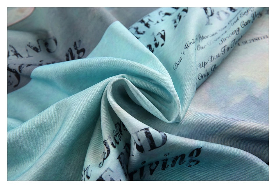 Close-up of the aqua shirt fabric gathered into folds, showing its cloudy pastel print and black lettering.