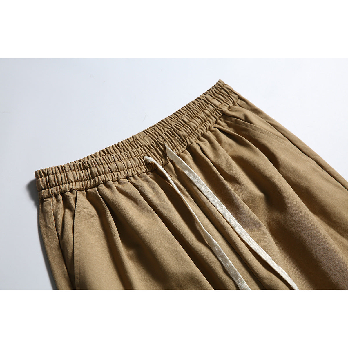Close-up of tan trousers showing the gathered elastic waistband, white drawstrings and front pleats.