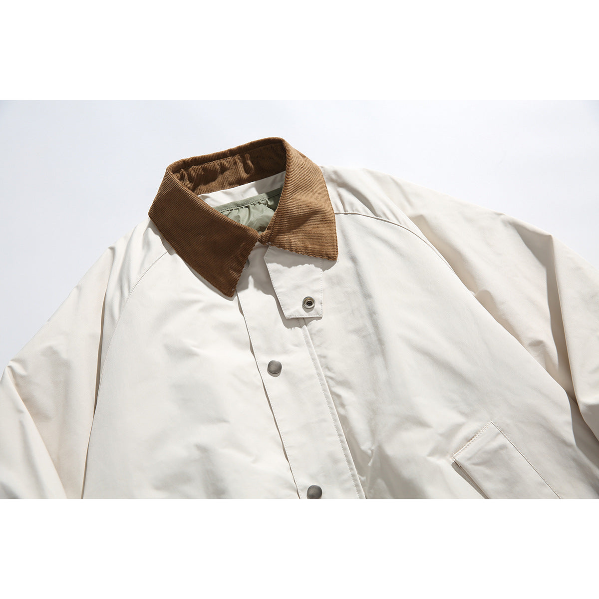 Close-up of an ivory jacket with a brown corduroy collar, snap-front placket, and angled pocket.