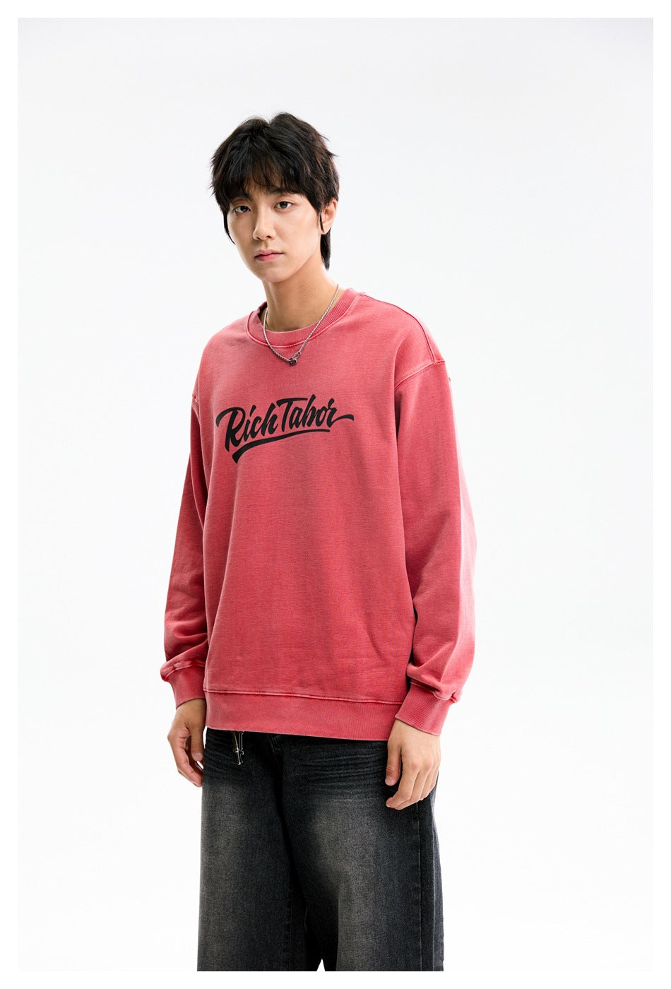 Model wearing a dusty-rose crewneck sweatshirt with black script chest print and black jeans.