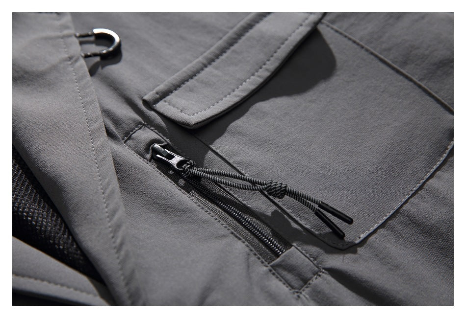 Close-up of the charcoal jacket's chest pocket, zipper with cord pulls, and small metal loop.