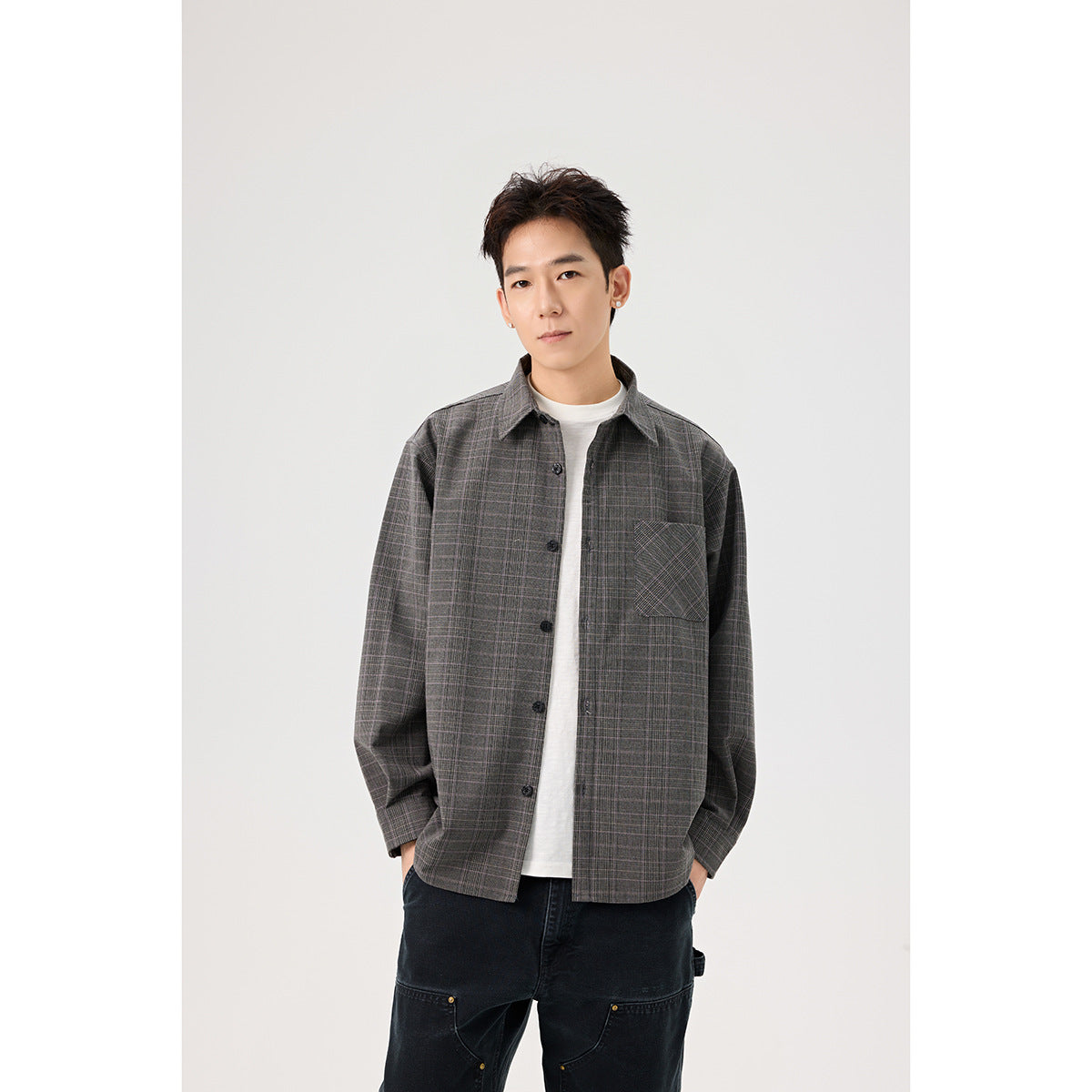 Closer front view of a model wearing a gray plaid overshirt with a button front and chest pocket over a white tee.