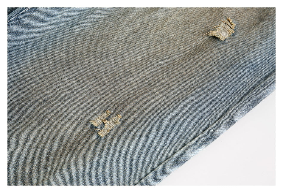 Close-up of light blue faded denim with two distressed patches and frayed threads.