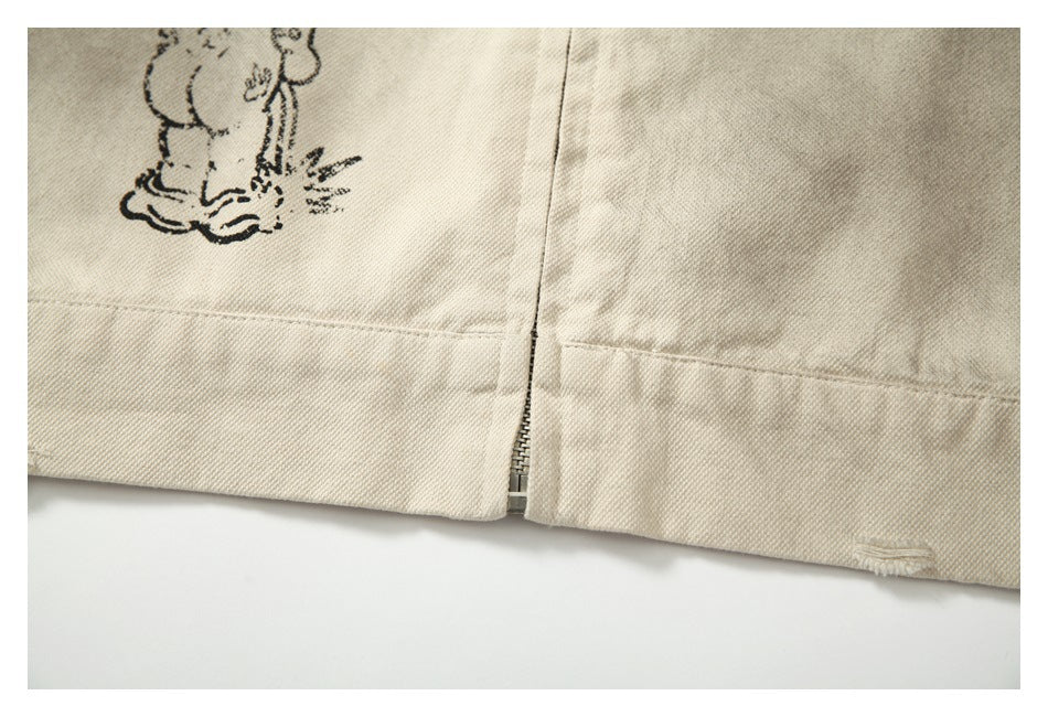 Close-up of the beige jacket hem with a short exposed zipper and part of a black cartoon print.