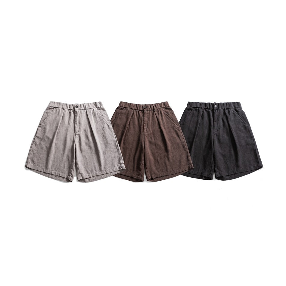 Three pairs of pleated shorts shown from the front in light gray, brown, and charcoal.
