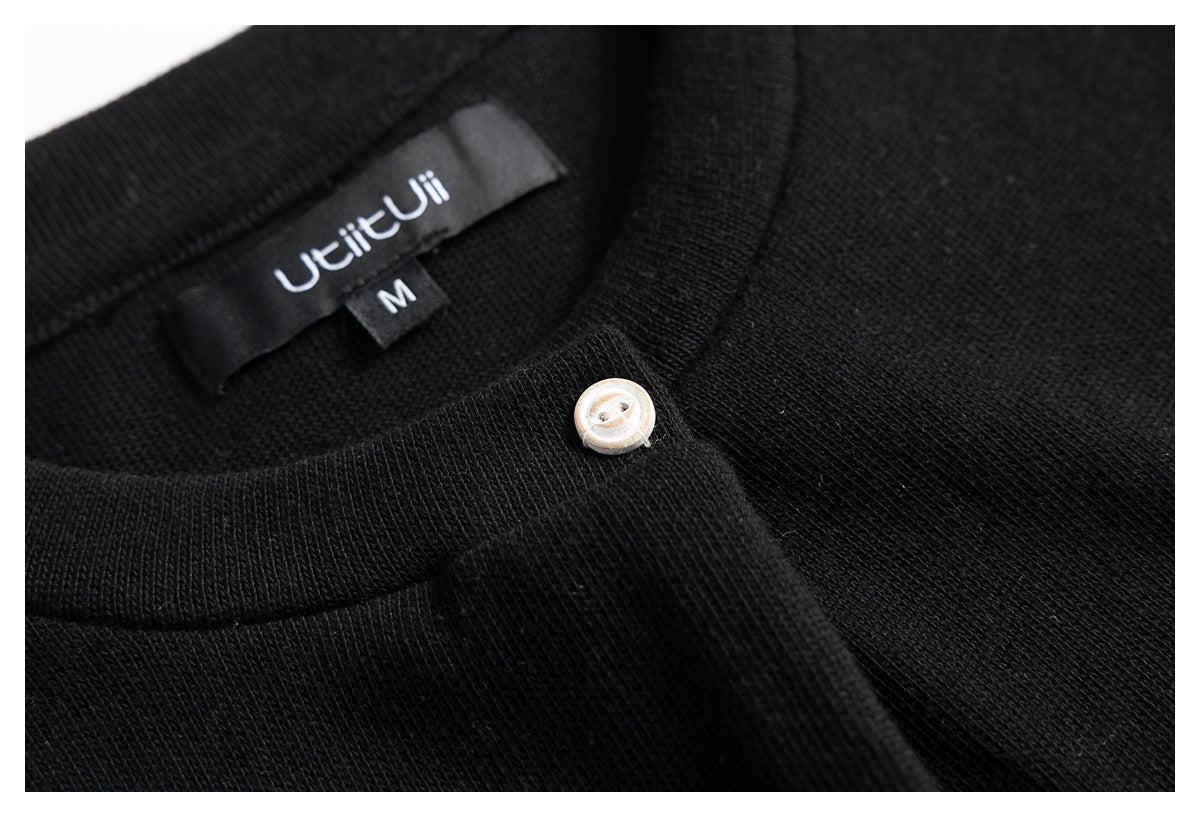 Close-up of a black knit neckline showing a sewn-in label marked M and a pale button.
