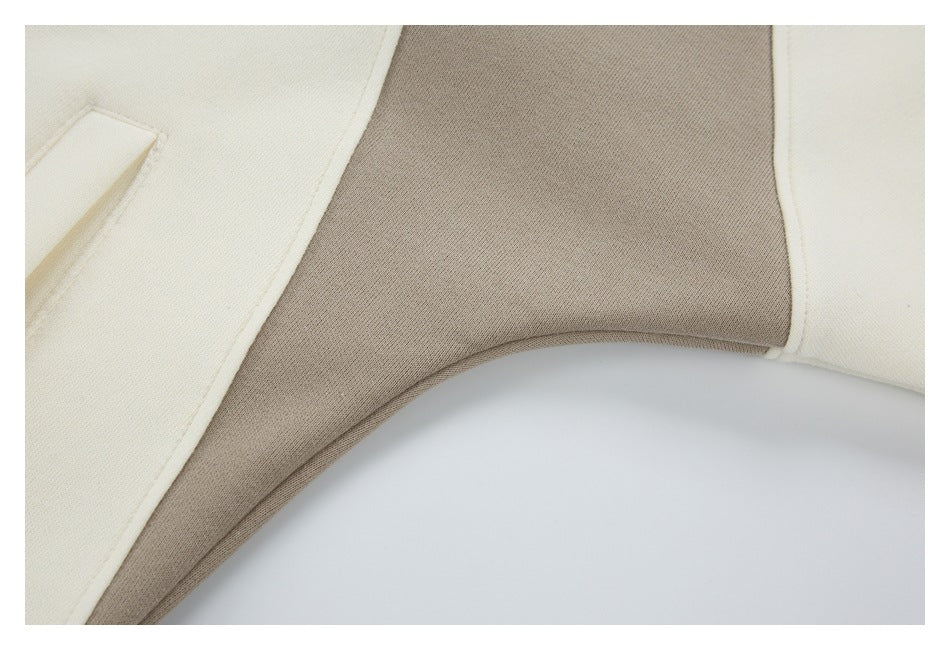 Close-up of the taupe side panel edged with cream piping on a cream color-block garment.