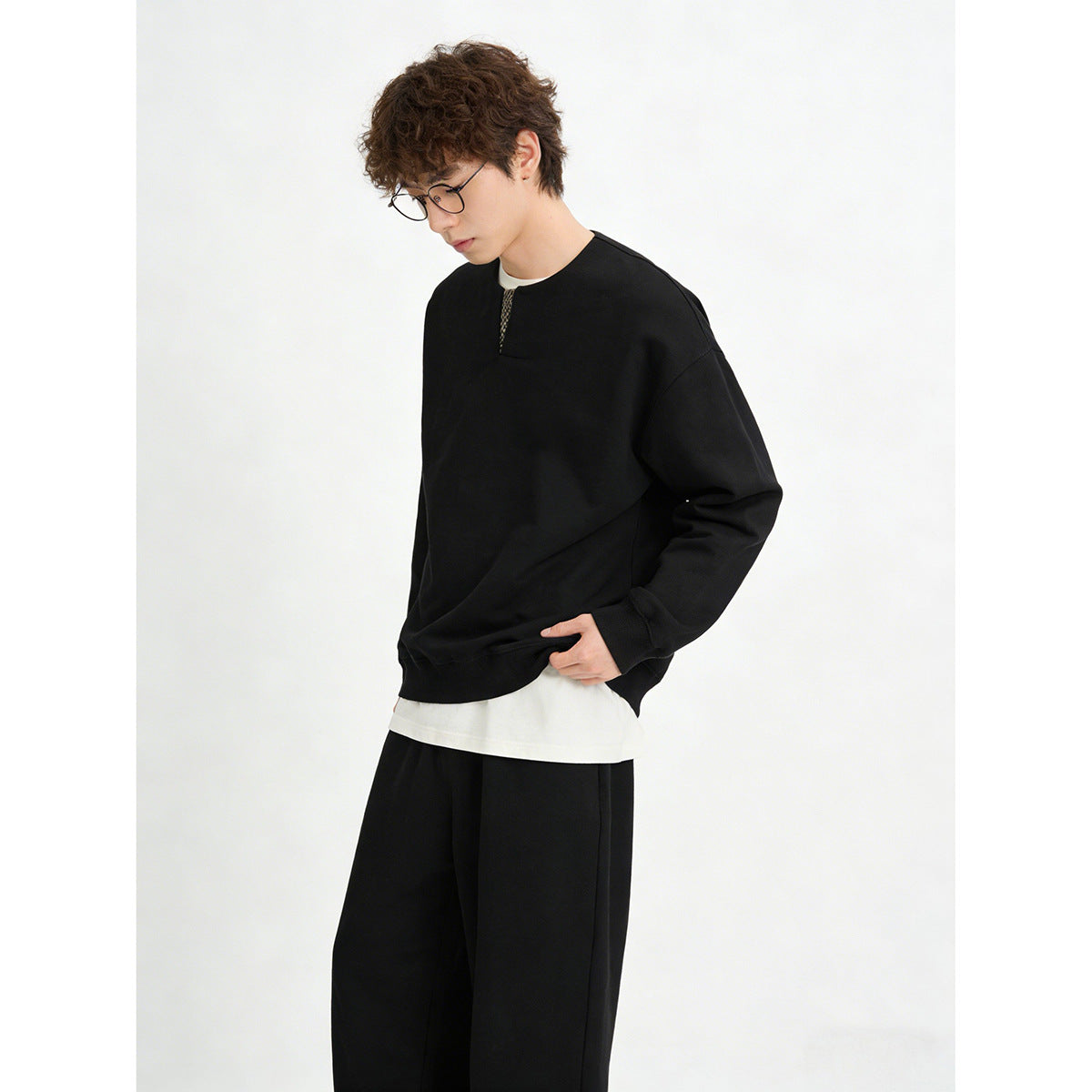 Model wearing a black long-sleeve sweatshirt with a small patterned neckline insert, layered over a white shirt.