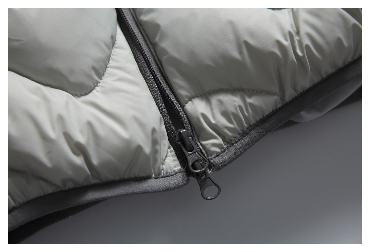 Close-up of a black two-way zipper and dark trim on a light gray quilted padded jacket.