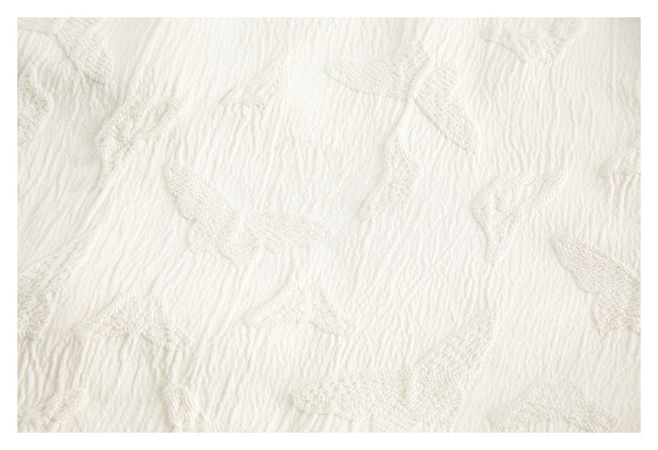 Close-up of cream-colored textured fabric with a raised leaf and floral pattern.