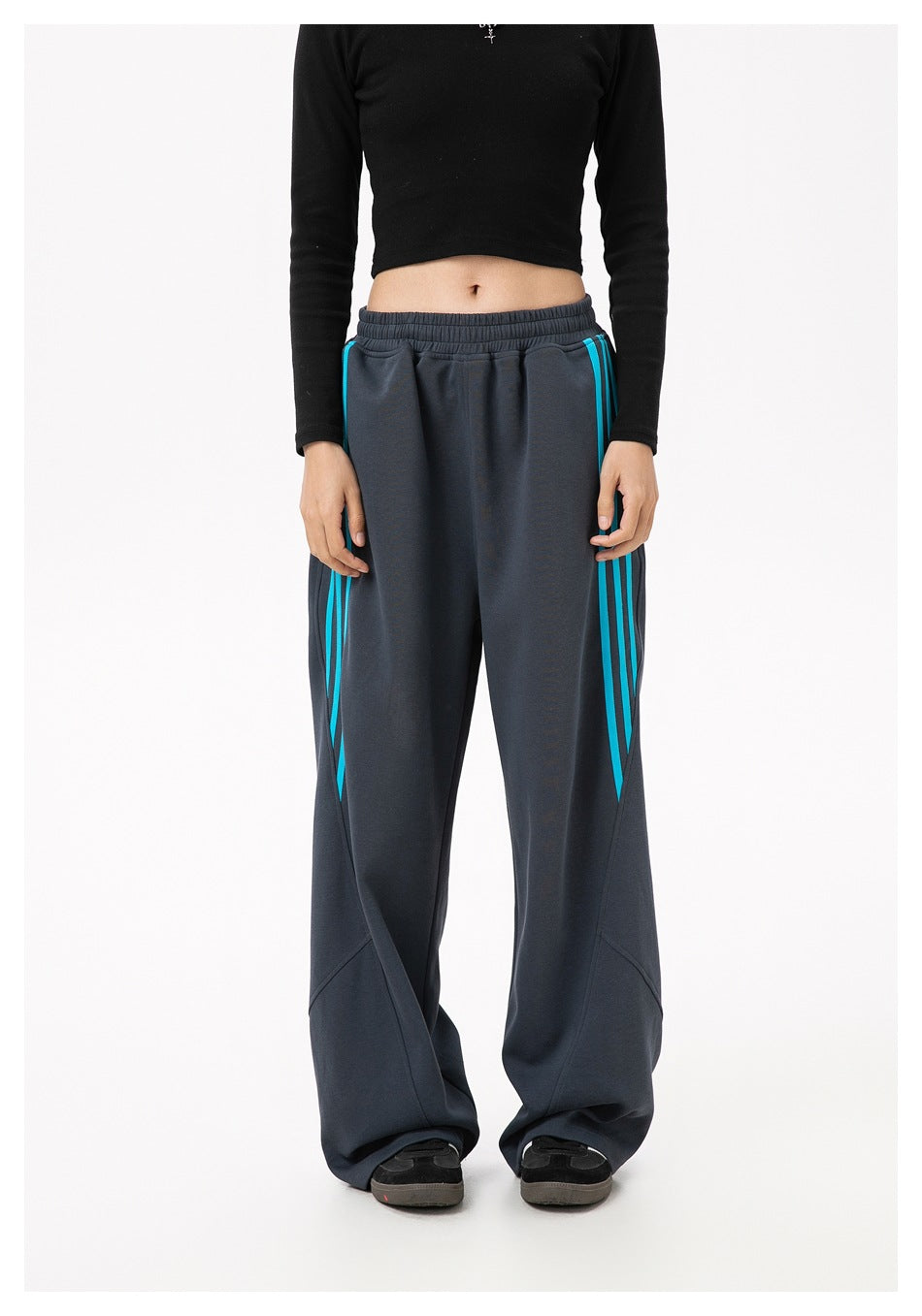 Model wearing dark gray wide-leg sweatpants with blue side stripes, cropped black top, front view
