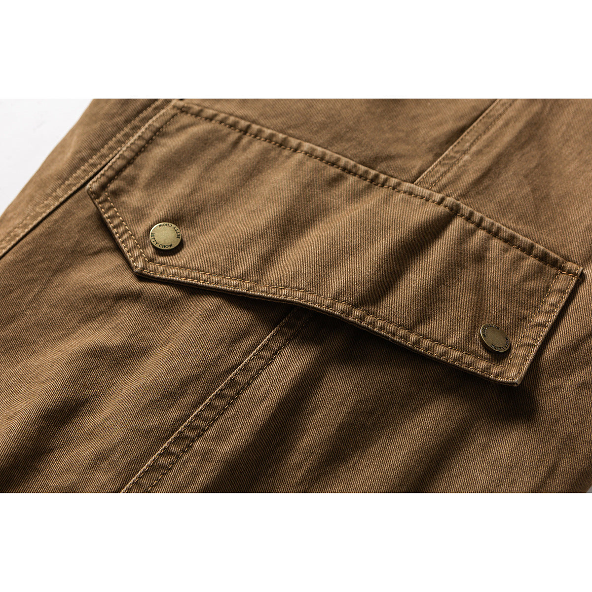 Close-up of a tan cargo pants pocket flap with two buttons and visible double stitching.
