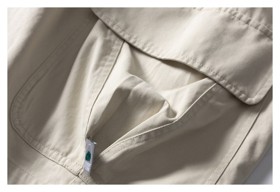 Close-up of a flap cargo pocket and sewn label on light beige shorts.