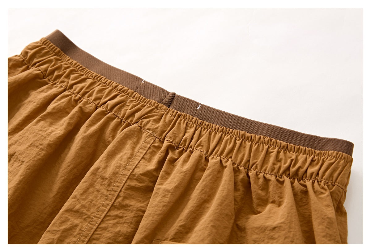 Close-up of camel-brown shorts with a gathered elastic waistband and brown ribbed band.